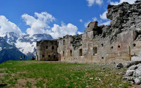 Rovine del forte Zaccarana, con montagne innevate sullo sfondo e cielo azzurro con nuvole bianche.