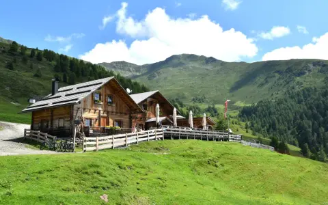 Rifugio in legno con tavoli all'aperto, ideale per un giro delle malghe in Val di Non. Montagne verdi e cielo azzurro.
