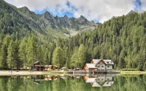 Riflessi sul lago alpino nella piana di Nambino, con boschi di conifere e montagne sullo sfondo.