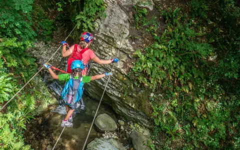 Bambini affrontano un emozionante percorso ponte tibetano tra rocce e vegetazione lussureggiante.