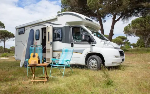 Un camper pronto per un tour in Trentino, con chitarra, cappello e sedie da campeggio in un prato verde.