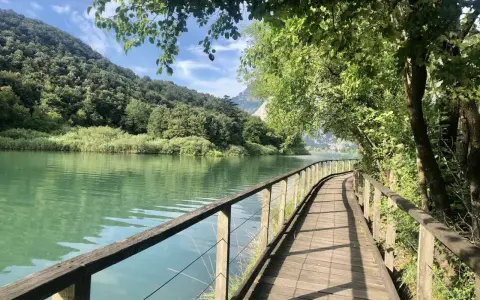 Sentiero in legno lungo il lago di Toblino, con montagne verdi sullo sfondo. Ideale per scoprire come arrivare.