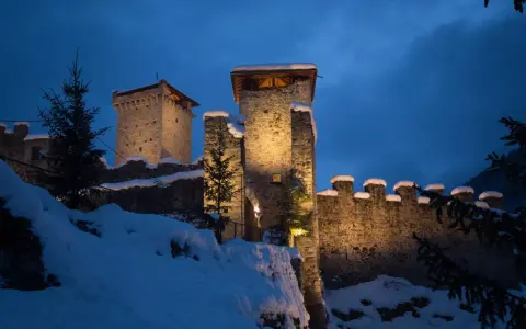 Castello innevato illuminato di notte, con alberi di Natale e luci che ricordano i mercatini di Natale di Ossana.