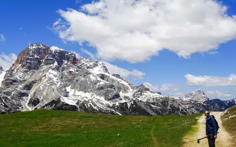 Un escursionista si ferma su un sentiero di montagna, con imponenti vette innevate sullo sfondo. Perfetti percorsi per camminare.