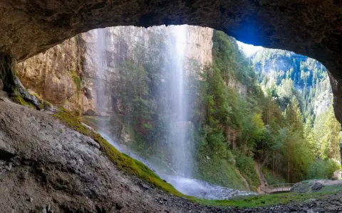 Vista da una grotta su maestose cascate del Trentino, con sentieri e ponticelli che invitano all'esplorazione.