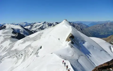 Alpinisti in cammino sulla cresta innevata del ghiacciaio Cevedale, con vette maestose sullo sfondo.