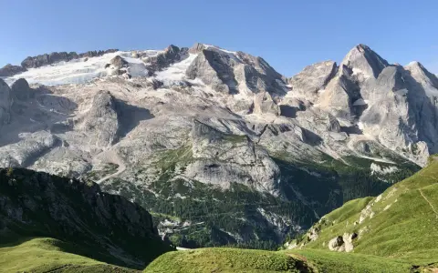 Vette innevate del Viel del Pan si stagliano maestose su un paesaggio alpino verdeggiante, con un piccolo borgo incastonato tra i boschi.