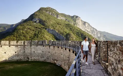 Coppia passeggia su un bastione di un castello con montagne verdi sullo sfondo. Un'esperienza da vivere nel Trentino da scoprire.