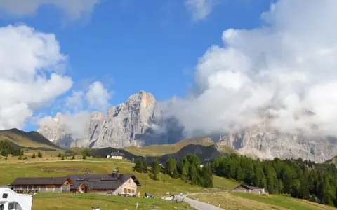 Panorami mozzafiato per escursioni a Passo Rolle. Rifugi alpini e vette imponenti sotto un cielo azzurro con nuvole bianche.