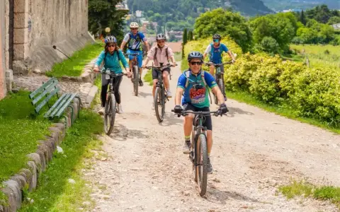 Gruppo di ciclisti su sentiero sterrato, godendosi gli eventi Trentino in un paesaggio verdeggiante.