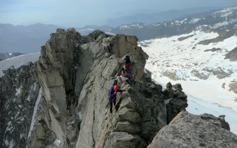 Alpinisti in cordata affrontano un crinale roccioso innevato, con la **cima Presanella** sullo sfondo.