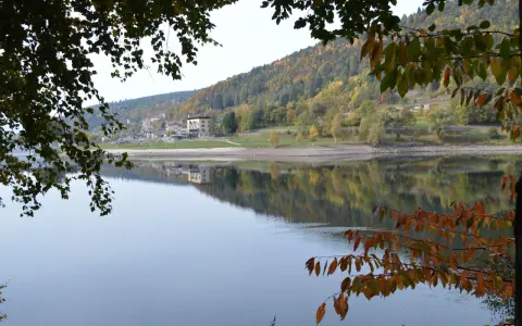 Autunno a Baselga di Pinè: il lago riflette le case e i boschi colorati. Cosa vedere in questo incantevole borgo trentino.