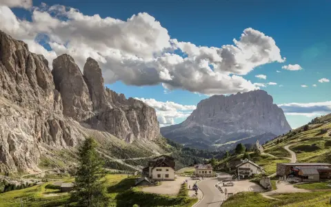 Panorami mozzafiato al Passo Gardena, con imponenti vette rocciose e un'altitudine che toglie il fiato. Case e strade si snodano tra i verdi pendii.