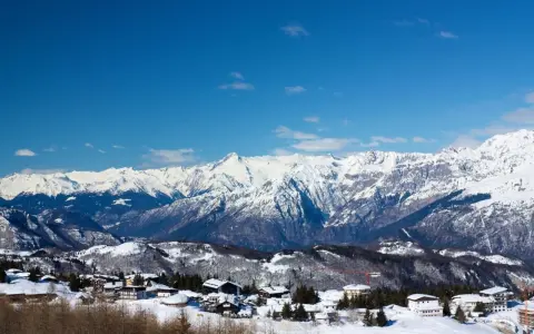 Paesaggio invernale con case innevate e montagne maestose sullo sfondo, un incantevole scenario al Passo Bondone.