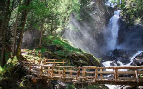 Sentiero in legno conduce alle maestose cascate Val di Sole, immerse in un bosco rigoglioso.