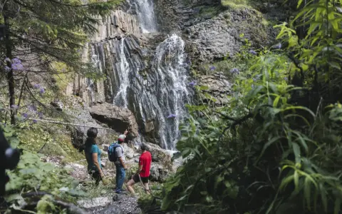 Escursionisti ammirano le spettacolari cascate schiavaneis, immerse nel verde e circondate da rocce basaltiche.