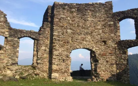 Rovine del castello di Altaguardia, con un uomo seduto che guarda il panorama.