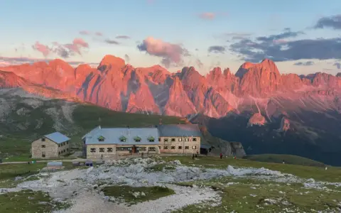 Rifugio sul **Monte Catinaccio** illuminato dal tramonto, con le vette rocciose che si tingono di rosa.