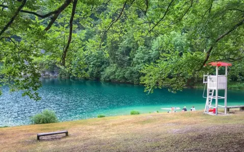 Rilassante **lago Lamar** con acque turchesi, bagnanti e torretta di salvataggio sotto alberi verdi.