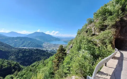 Vista panoramica dal Monte Vezzena con lago azzurro e montagne sullo sfondo. Strada con galleria scavata nella roccia.