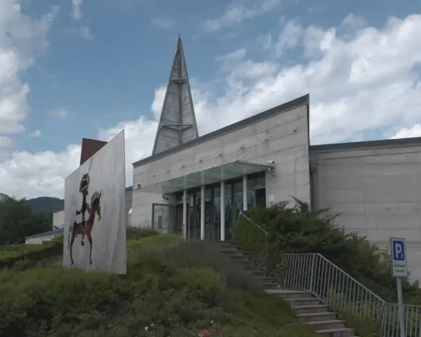 Il museo retico, con la sua architettura moderna e un'installazione artistica di un guerriero a cavallo, si erge sotto un cielo nuvoloso.