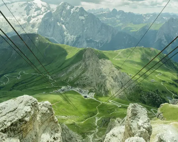 Vista mozzafiato da Canazei al Passo Sella, con funivia che attraversa verdi pendii e imponenti vette dolomitiche.