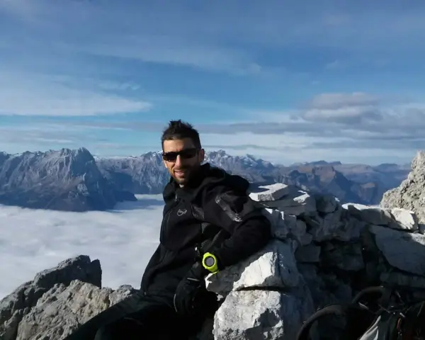 Uomo in vetta con abbigliamento tecnico, ideale per capire come vestirsi in montagna a settembre. Paesaggio alpino mozzafiato.