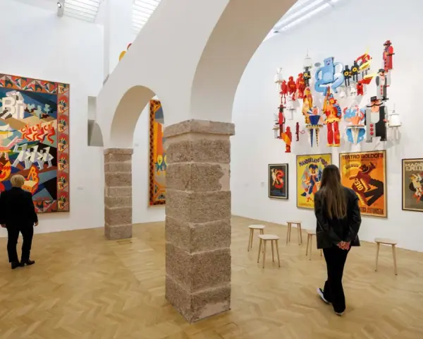 Un visitatore ammira un arazzo colorato e installazioni futuristiche al muse rovereto.