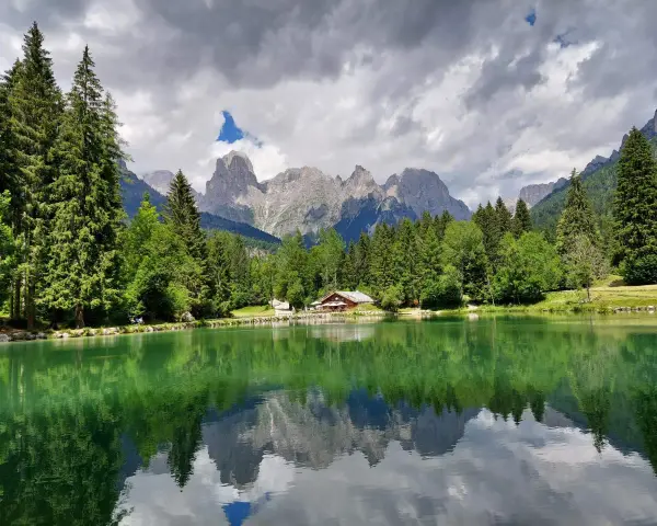 Riflessi alpini sul lago di Passo Cereda. Montagne imponenti e boschi verdi incorniciano un tranquillo specchio d'acqua.
