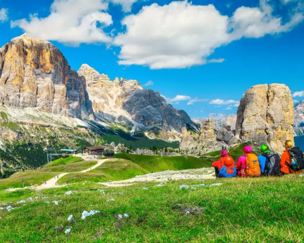 Quattro escursionisti ammirano le maestose Dolomiti Trentino Alto Adige, con cime imponenti e un cielo azzurro.
