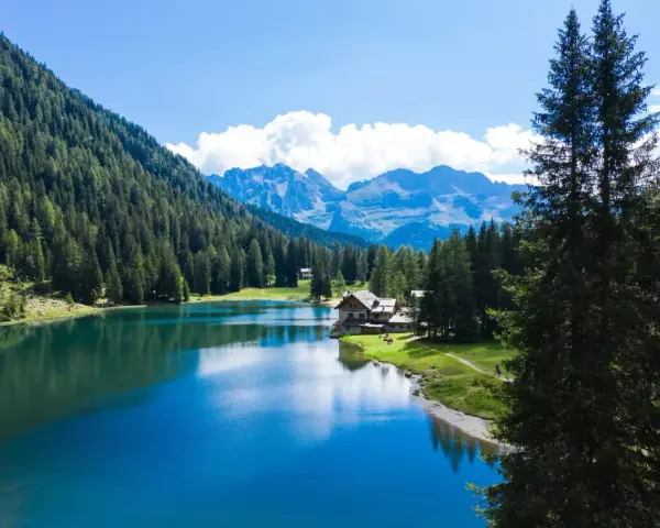 Incantevole lago alpino vicino a Madonna di Campiglio, con boschi rigogliosi, montagne maestose e un rifugio accogliente.