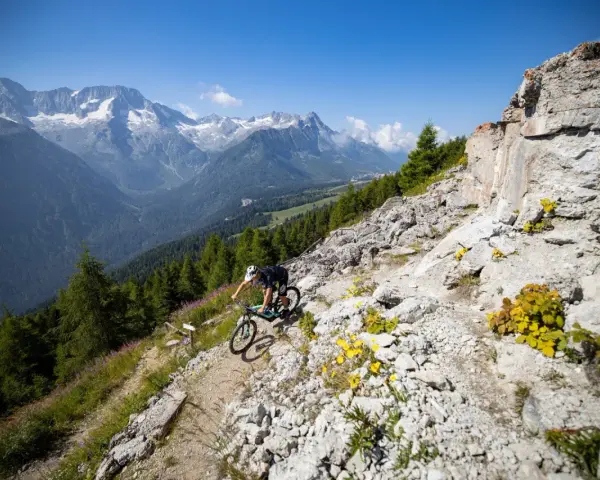 Ciclista in discesa su sentiero roccioso, con montagne innevate sullo sfondo, durante il giro dei forti tonale.