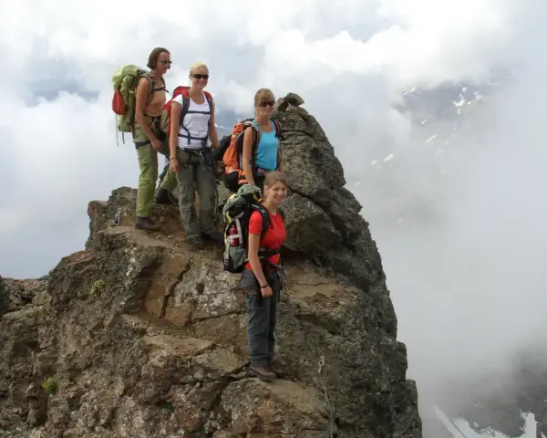 Quattro escursionisti con zaini si fermano sulla cima rocciosa di Cima Sternai, circondati da nuvole e nebbia.