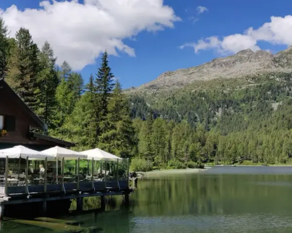 Rifugio in legno con tavoli all'aperto sul lago, circondato da boschi e montagne. Un luogo incantevole per scoprire cosa vedere a Pellizzano.