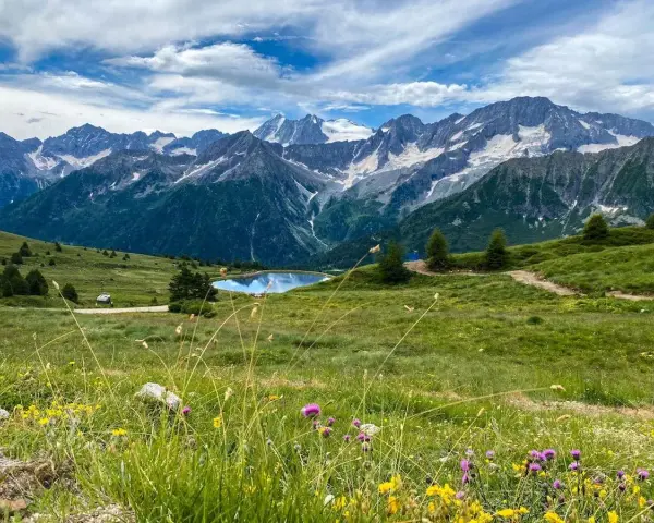 Un incantevole passo tra Lombardia e Trentino, con un lago alpino specchiato e montagne innevate sullo sfondo.