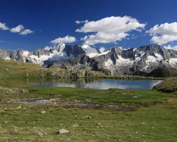 Laghi Val di Sole raggiungibili in auto: specchio d'acqua alpino con montagne innevate sullo sfondo e cielo azzurro con nuvole bianche.
