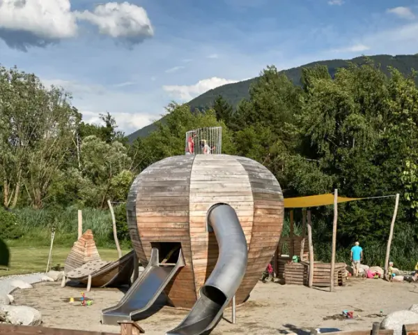 Un colorato parco giochi Trentino con una struttura a forma di sfera in legno, scivoli e bambini che giocano.