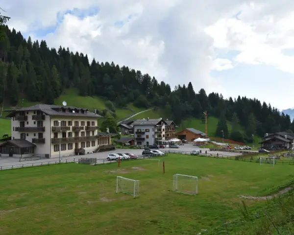 Edifici alpini e un campo da calcio con porte, immersi nel verde e circondati da boschi. La **passo Cereda altitudine** offre uno scenario incantevole.