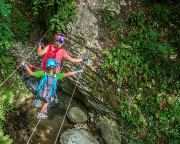 Bambini affrontano un emozionante percorso ponte tibetano tra rocce e vegetazione lussureggiante.