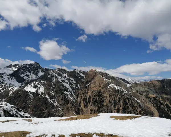 Cimon di Bolentina, un maestoso panorama montuoso con cime innevate e un cielo azzurro punteggiato di nuvole bianche.