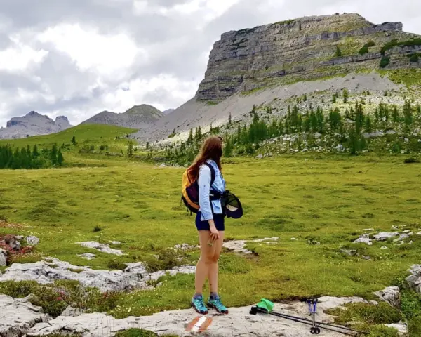 Ragazza con zaino ammira un paesaggio alpino con un imponente turrion basso.