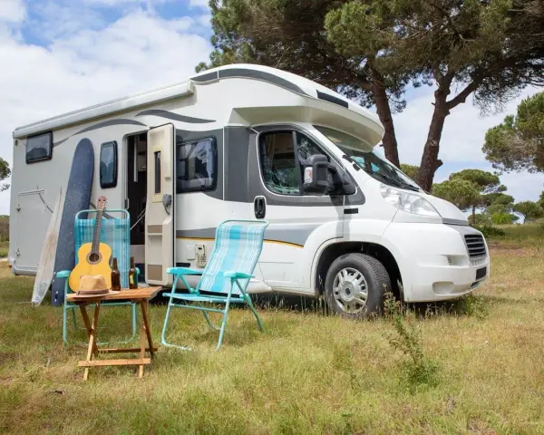 Un camper pronto per un tour in Trentino, con chitarra, cappello e sedie da campeggio in un prato verde.