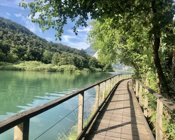 Sentiero in legno lungo il lago di Toblino, con montagne verdi sullo sfondo. Ideale per scoprire come arrivare.