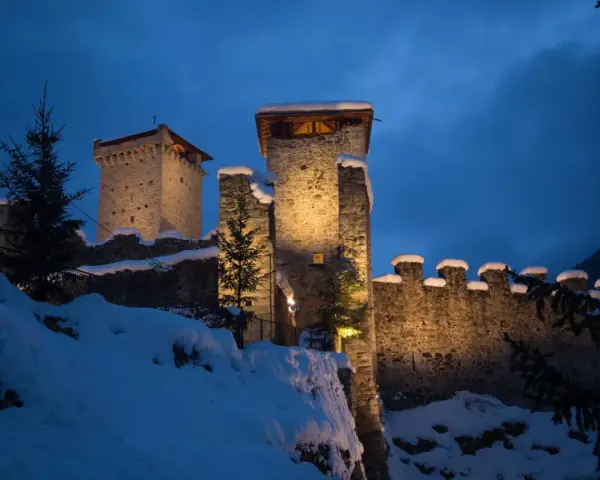 Castello innevato illuminato di notte, con alberi di Natale e luci che ricordano i mercatini di Natale di Ossana.