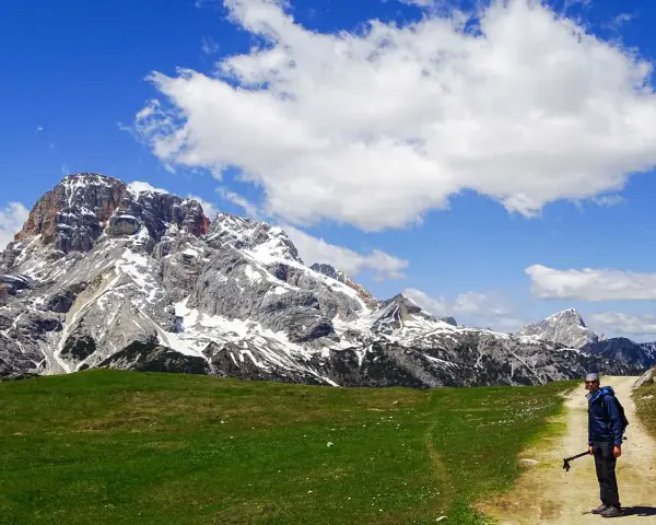 Un escursionista si ferma su un sentiero di montagna, con imponenti vette innevate sullo sfondo. Perfetti percorsi per camminare.