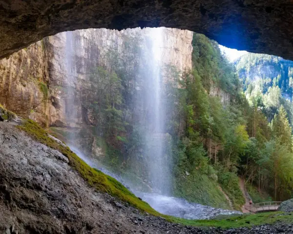 Vista da una grotta su maestose cascate del Trentino, con sentieri e ponticelli che invitano all'esplorazione.