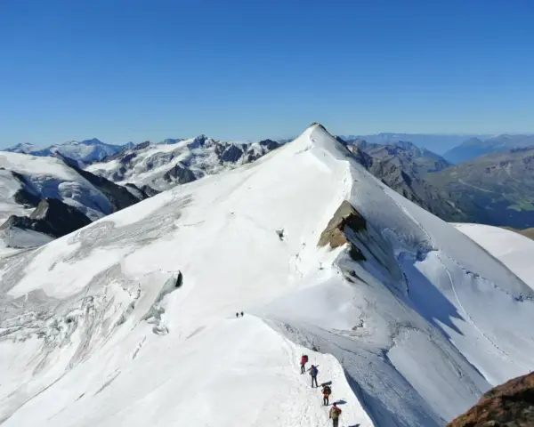 Alpinisti in cammino sulla cresta innevata del ghiacciaio Cevedale, con vette maestose sullo sfondo.