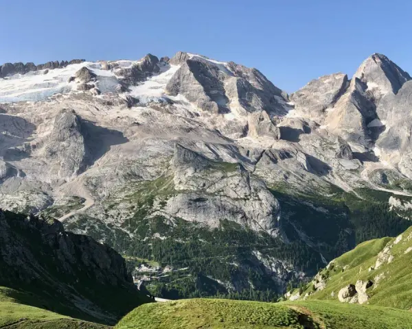 Vette innevate del Viel del Pan si stagliano maestose su un paesaggio alpino verdeggiante, con un piccolo borgo incastonato tra i boschi.