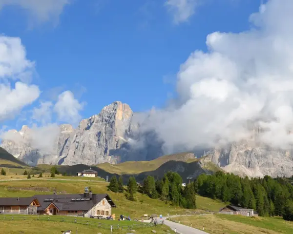Panorami mozzafiato per escursioni a Passo Rolle. Rifugi alpini e vette imponenti sotto un cielo azzurro con nuvole bianche.