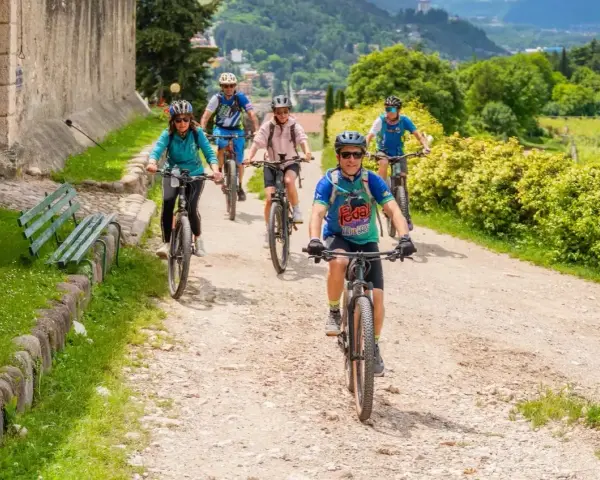 Gruppo di ciclisti su sentiero sterrato, godendosi gli eventi Trentino in un paesaggio verdeggiante.